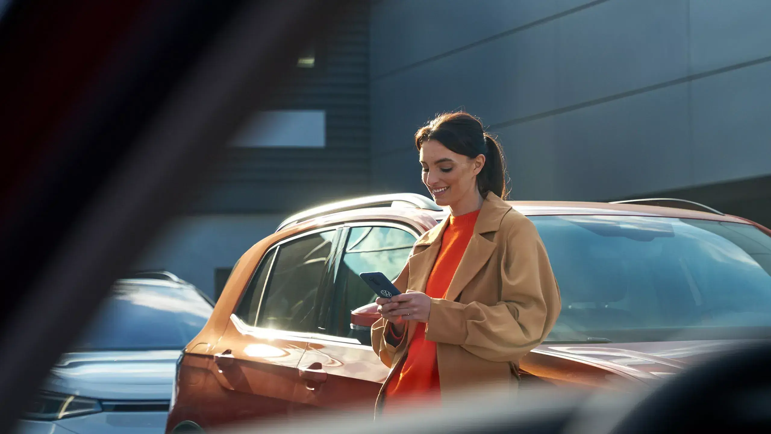 En kvinde læner sig op af en bil og kigger smilende på sin telefon