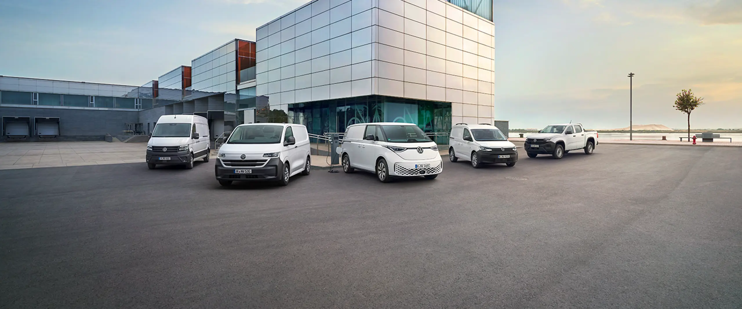 5 erhvervsbiler samlet foran bygning ved vandet